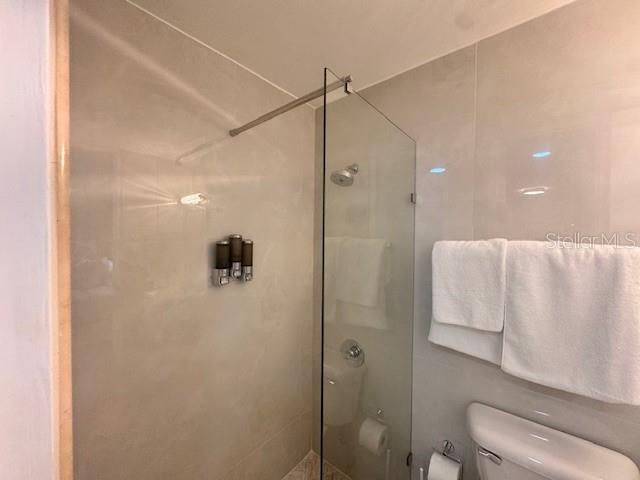 A bathroom features a glass-enclosed walk-in shower with wall-mounted dispensers and a nearby toilet — Ocean Drive 100 UNIT 806, LUQUILLO, PR
