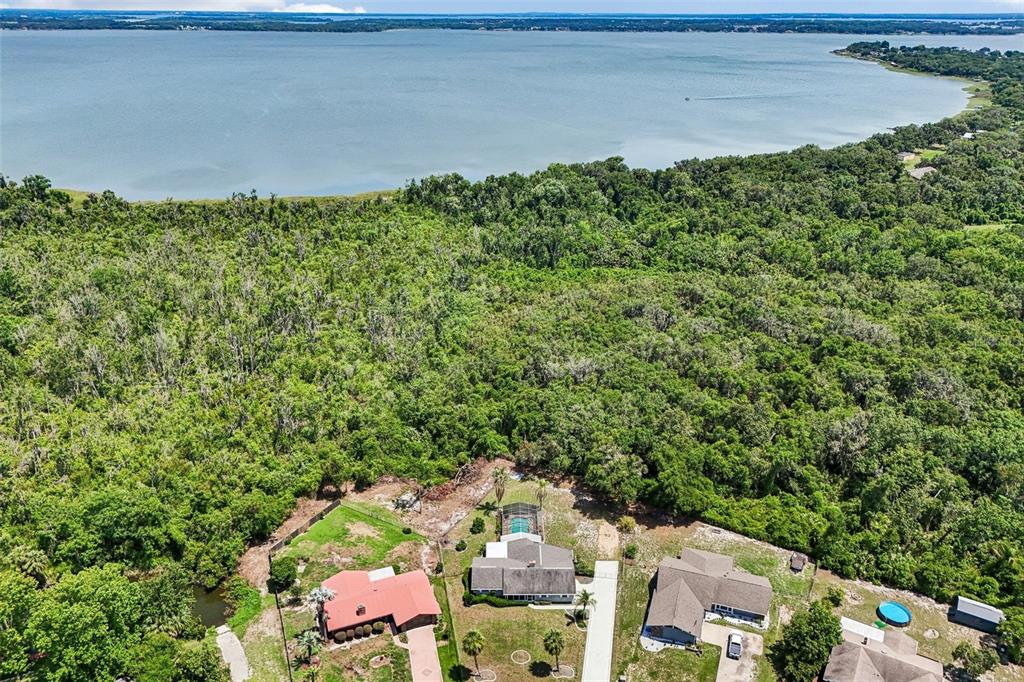An aerial view shows three houses situated near a dense forest bordering a large lake — 5234 MAGNOLIA TERRACE, FRUITLAND PARK, FL