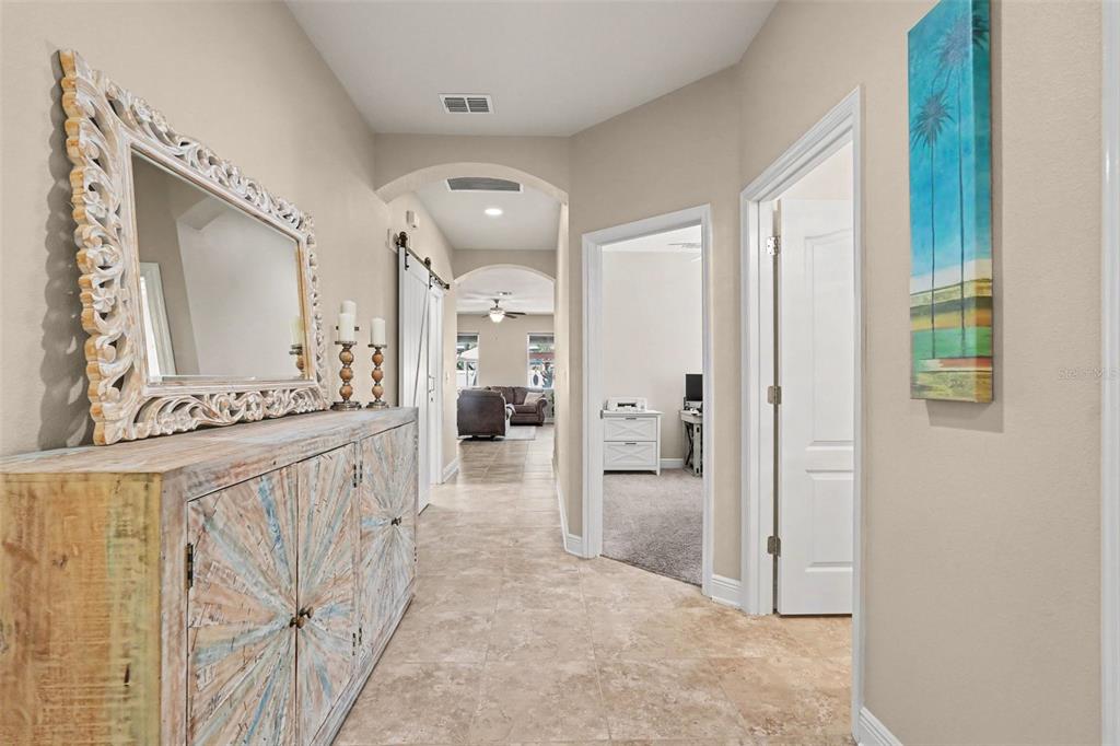 A hallway with tile flooring, a decorative wooden cabinet, a large mirror, and open doorways — 7703 S SPARKMAN STREET, TAMPA, FL