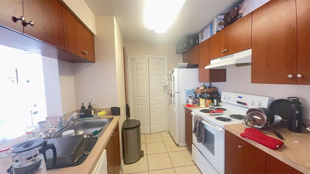 A kitchen features wooden cabinets, white appliances, a stainless steel sink, and tiled flooring — 2550 N ALAFAYA TRAIL UNIT 2111, ORLANDO, FL
