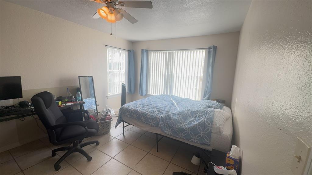 A bedroom with tile flooring, a bed, a desk with a chair, and vertical blinds — 2550 N ALAFAYA TRAIL UNIT 2111, ORLANDO, FL