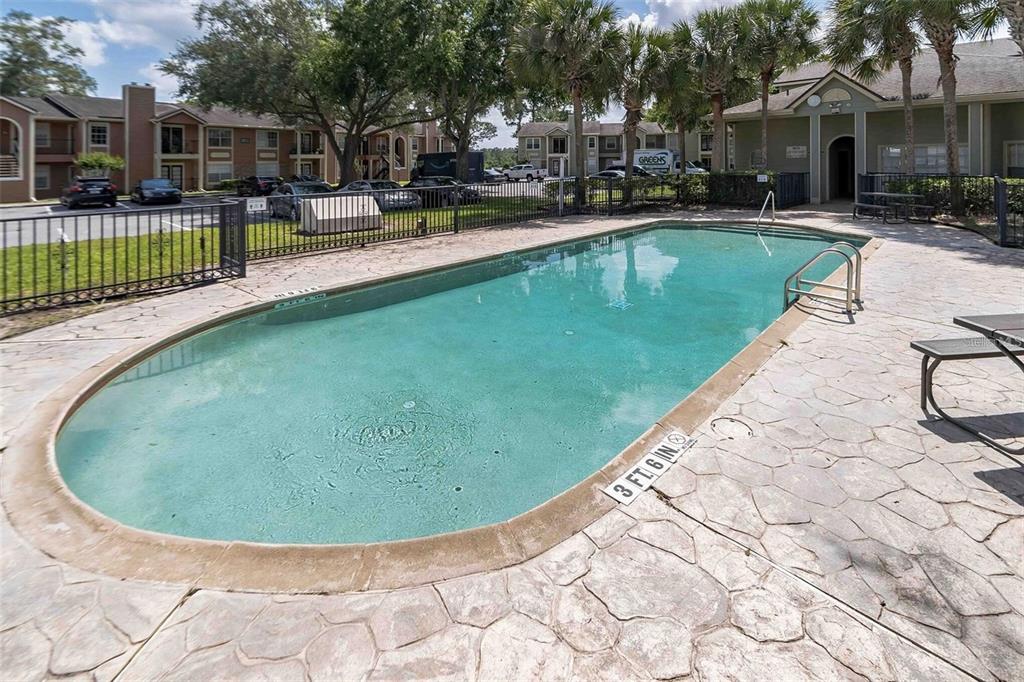 An outdoor swimming pool with a concrete deck is surrounded by apartment buildings and trees — 2550 N ALAFAYA TRAIL UNIT 2111, ORLANDO, FL