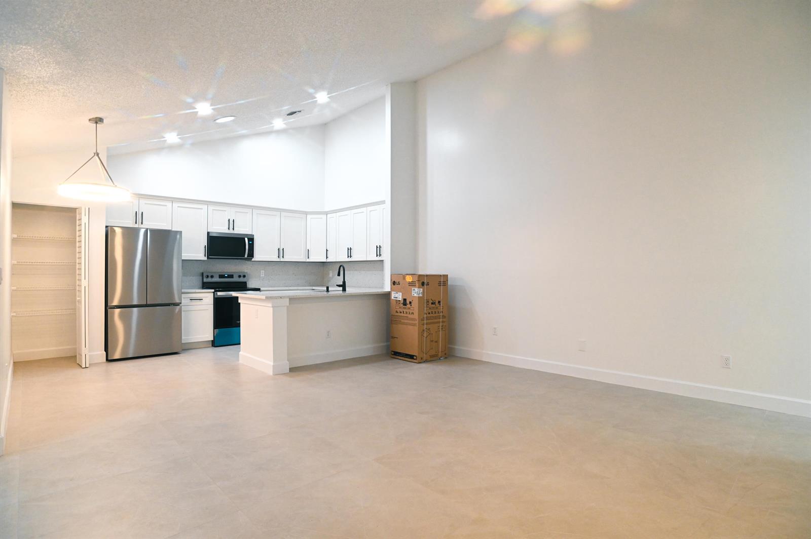 A kitchen with white cabinets, stainless steel appliances, and a large open living area — 1148 Summit Trail Circle # D, West Palm Beach FL 33415, WEST PALM BEACH, FL