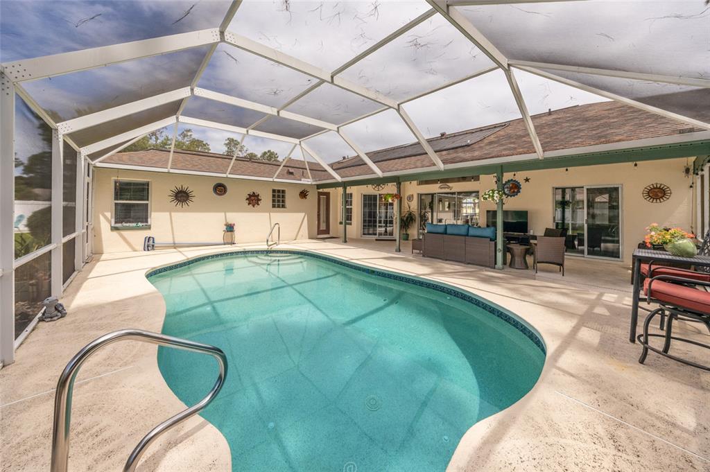 A screened-in patio features a swimming pool, outdoor seating, and beige concrete decking — 29 WOODHOLME LANE, PALM COAST, FL