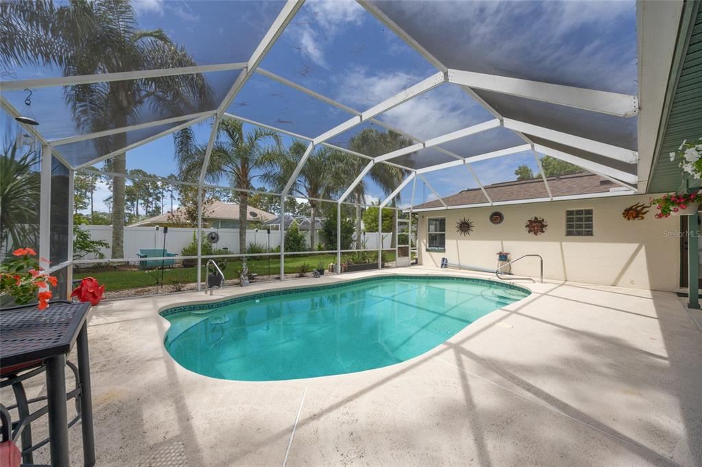 A swimming pool with a screen enclosure sits on a concrete patio behind a house — 29 WOODHOLME LANE, PALM COAST, FL