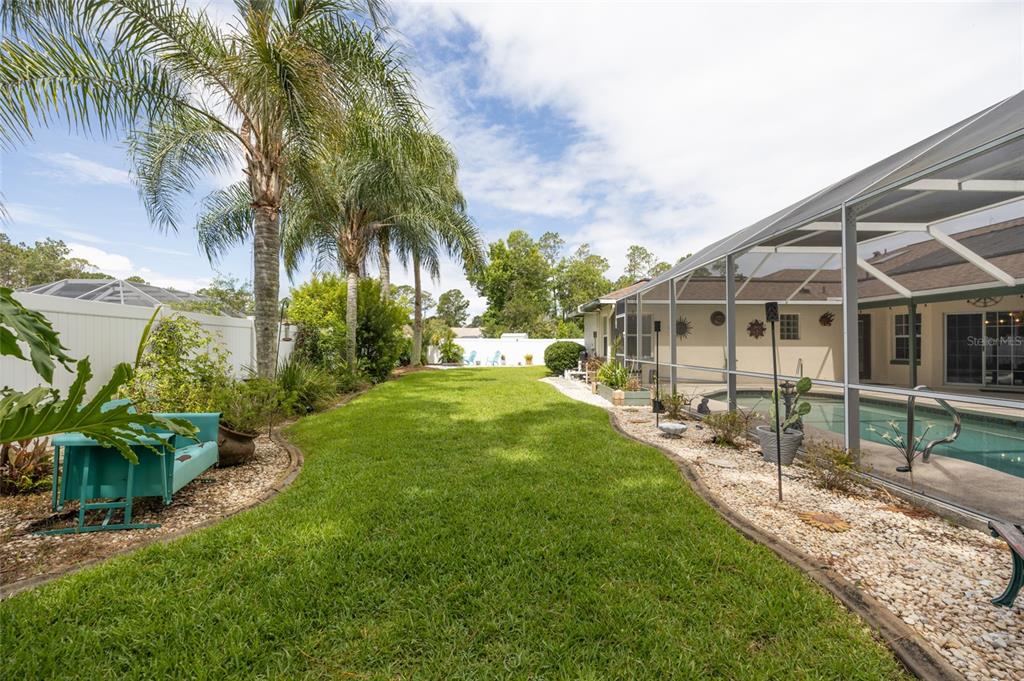 A backyard features a grassy lawn, a screened-in pool, and palm trees under a blue sky — 29 WOODHOLME LANE, PALM COAST, FL