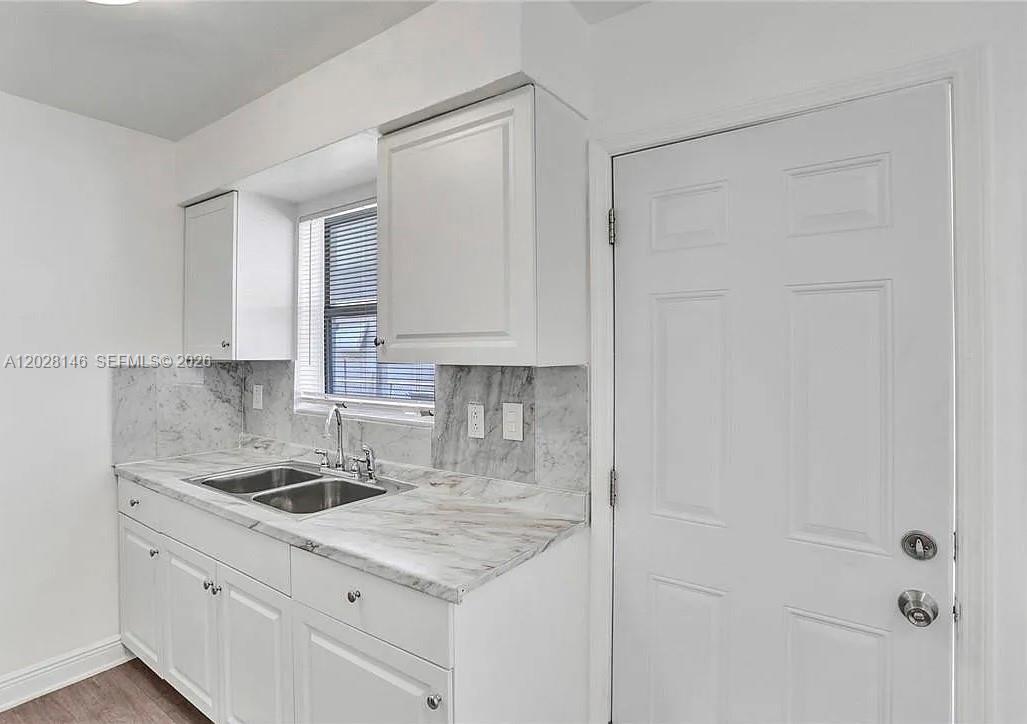 A kitchen features white cabinets, a marble-patterned countertop, a double sink, and a white door — 2627 Lincoln St, Hollywood FL 33020, HOLLYWOOD, FL