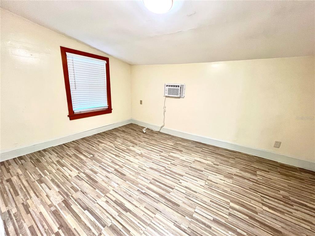 An empty room features light-colored walls, wood-look flooring, a window with blinds, and a wall-mounted air conditioner — 343 WEAVER AVENUE, LAKE WALES, FL