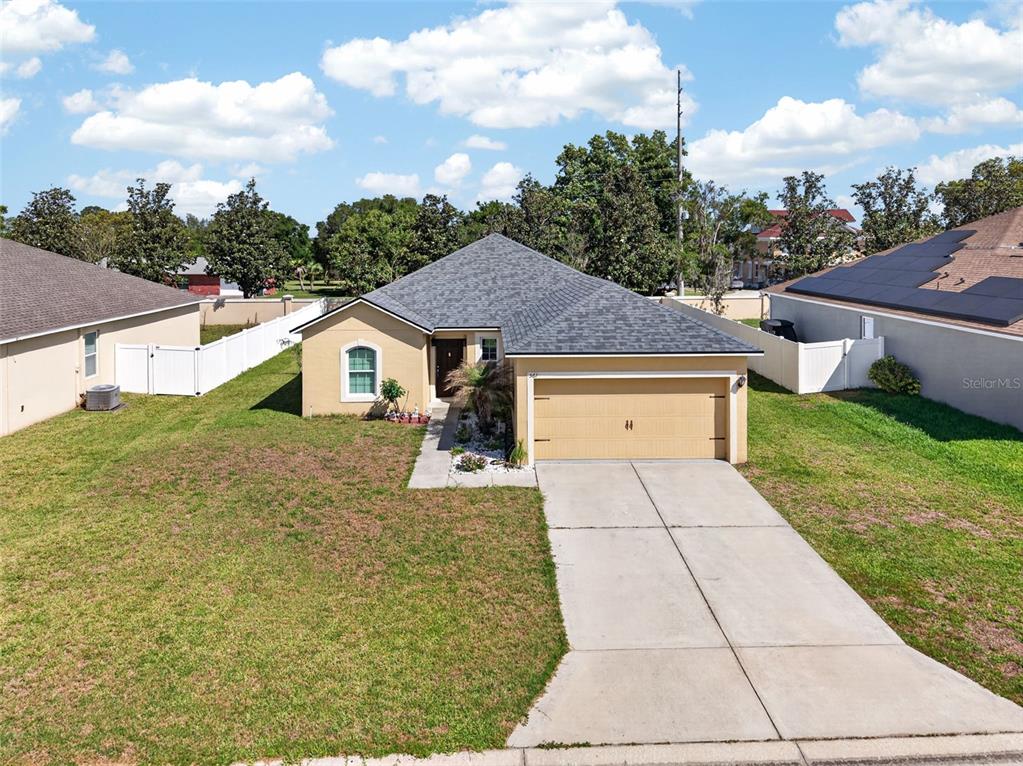 An aerial view shows a single-story house with a tan exterior, shingled roof, and garage — 561 LAKE CUMMINGS WAY, LAKE ALFRED, FL