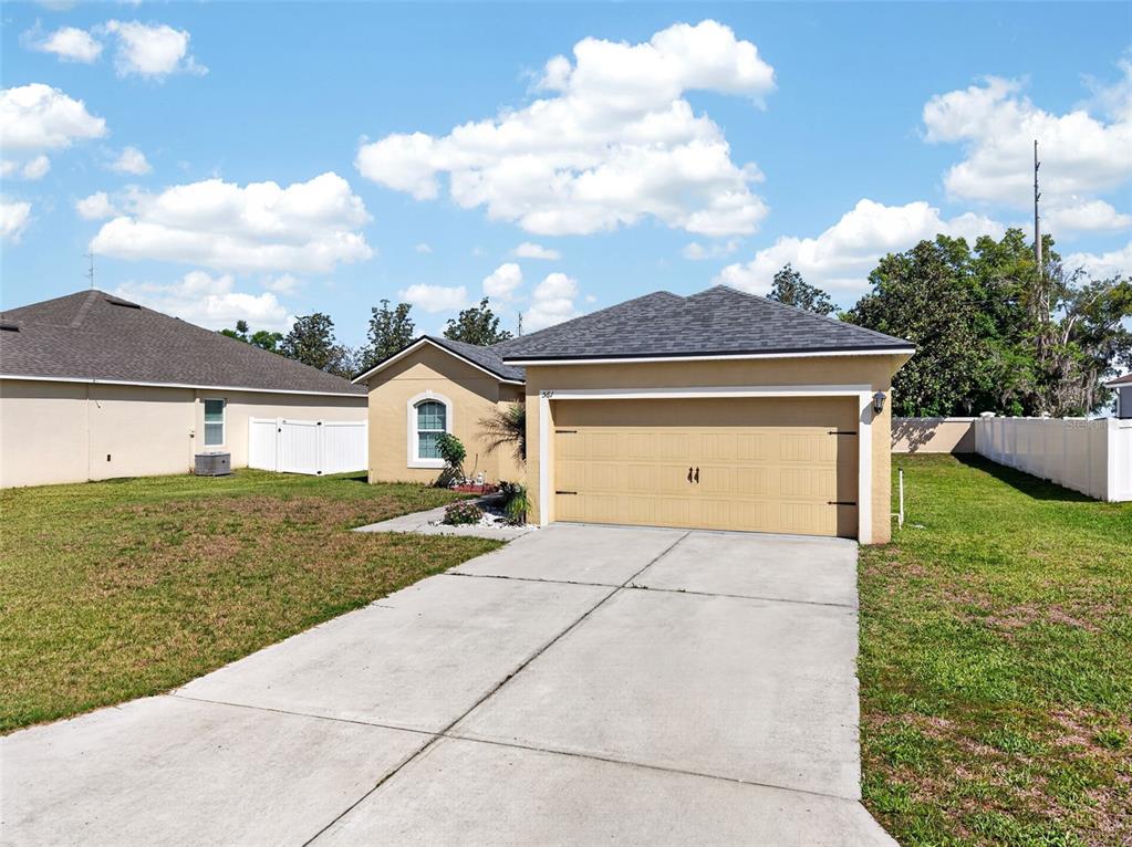 A tan single-story house with a two-car garage and a concrete driveway under a blue sky — 561 LAKE CUMMINGS WAY, LAKE ALFRED, FL