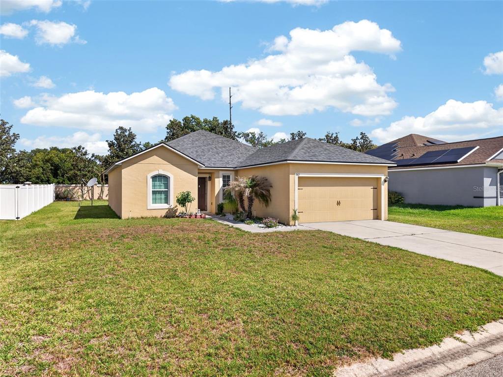A single-story tan house with a two-car garage and a white vinyl fence — 561 LAKE CUMMINGS WAY, LAKE ALFRED, FL