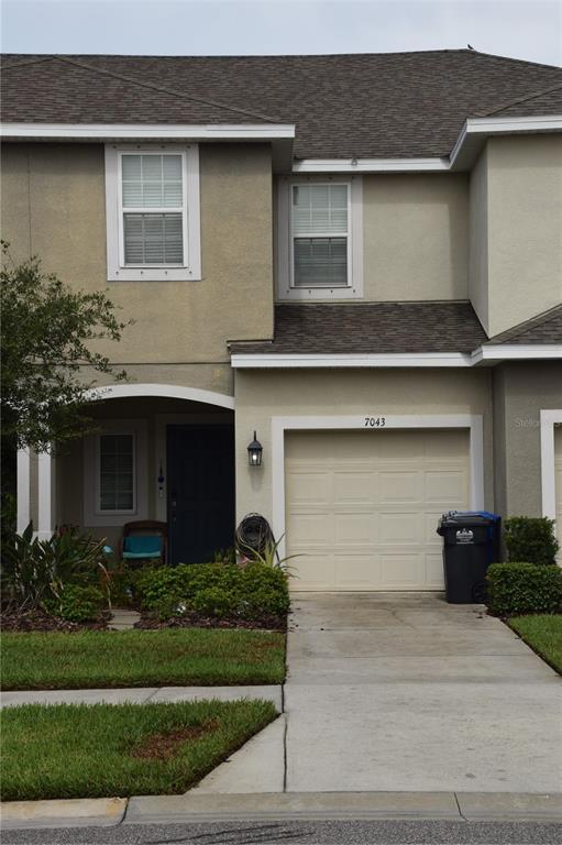 A two-story townhouse exterior features a single-car garage, a covered entryway, and a concrete driveway — 7043 SUMMER HOLLY PLACE, RIVERVIEW, FL