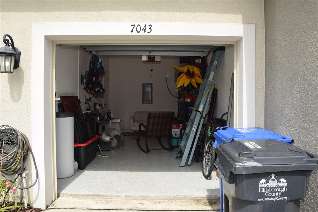 A garage with a concrete floor, a rocking chair, a ladder, and two trash bins — 7043 SUMMER HOLLY PLACE, RIVERVIEW, FL