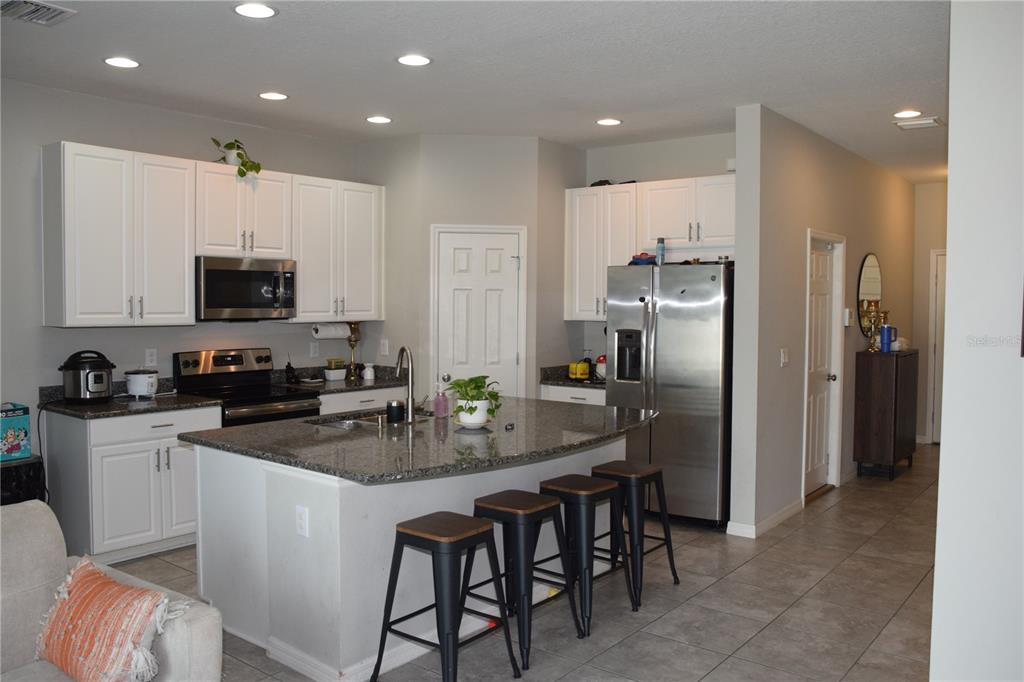 A kitchen features white cabinets, granite countertops, a stainless steel refrigerator, and a breakfast bar — 7043 SUMMER HOLLY PLACE, RIVERVIEW, FL