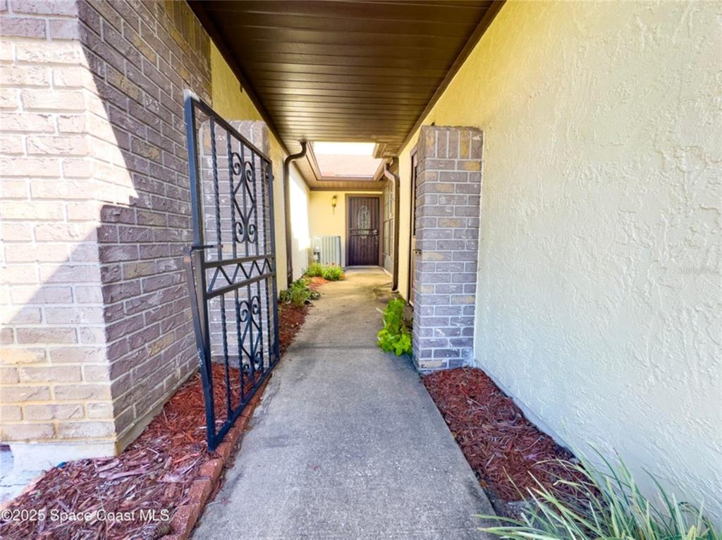 A concrete walkway leads to a front door through a covered entryway with brick pillars — 2193 KINGS CROSS STREET, TITUSVILLE, FL