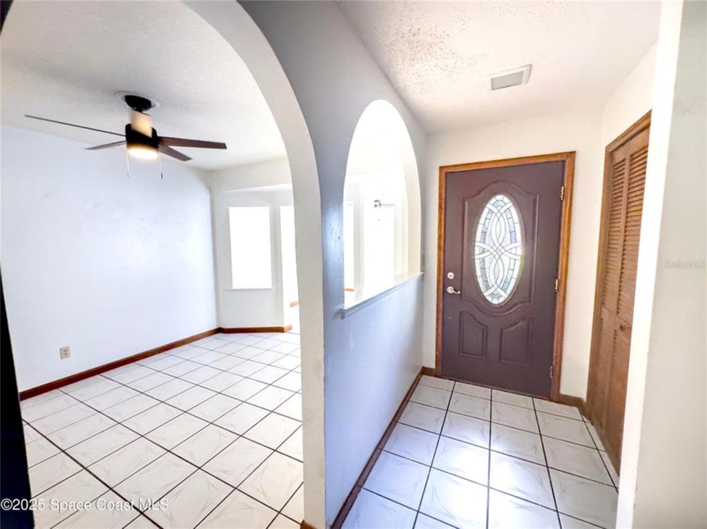 An entryway with a dark front door leads to a tiled room with an arched opening — 2193 KINGS CROSS STREET, TITUSVILLE, FL