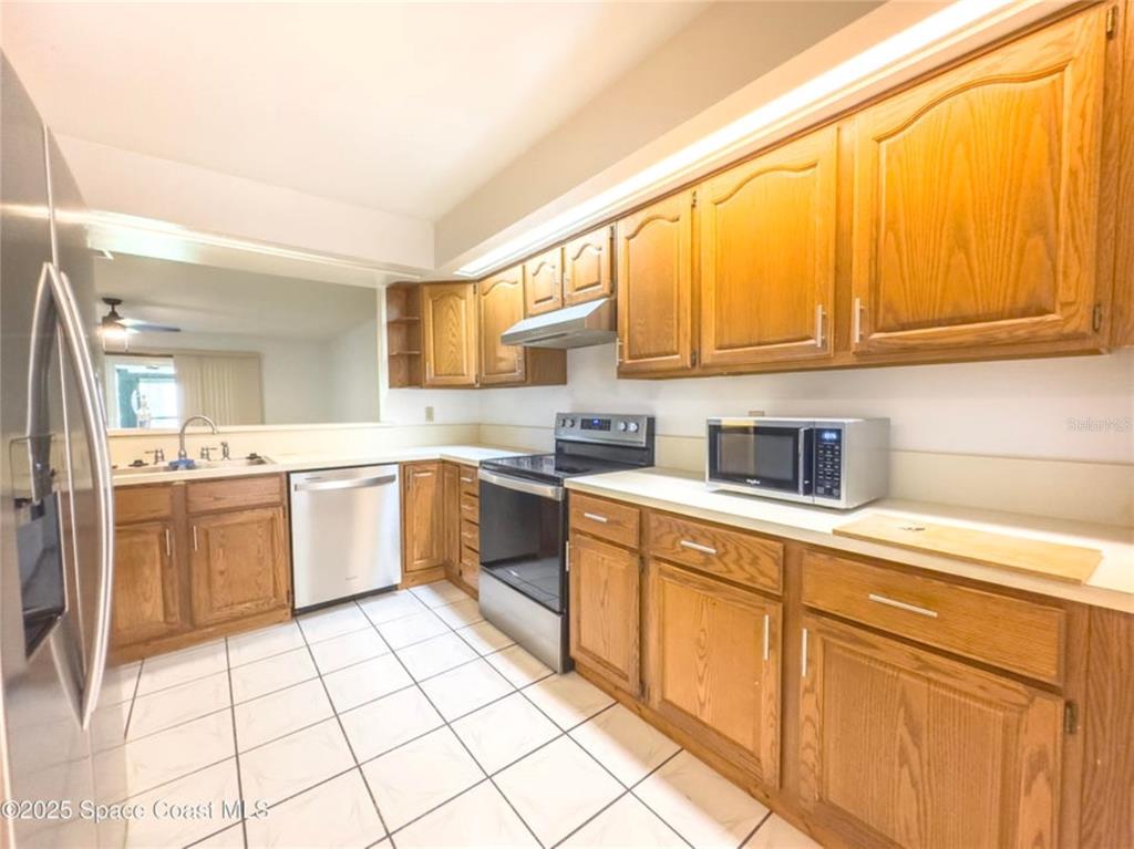 A kitchen features oak cabinets, stainless steel appliances, and white tile flooring — 2193 KINGS CROSS STREET, TITUSVILLE, FL