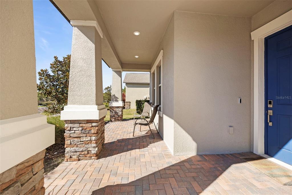 A covered front porch features a brick paver floor, stone-based columns, and a blue door — 3138 HILLIARD DRIVE, WESLEY CHAPEL, FL