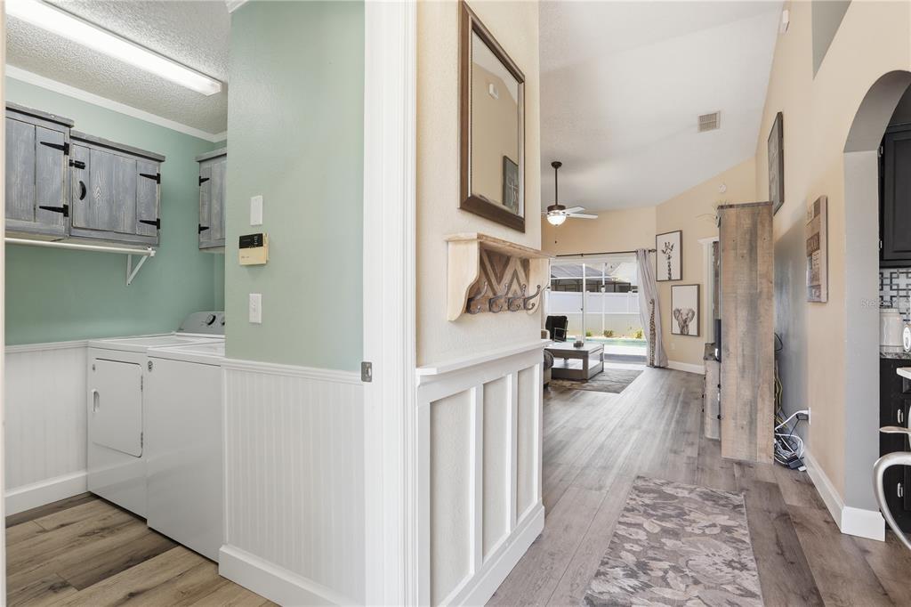 A laundry room with light green walls and white wainscoting opens into a living area — 844 WOODSONG WAY, CLERMONT, FL