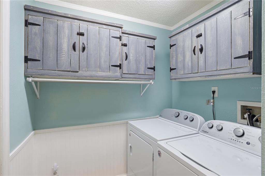 A laundry room features light blue walls, white wainscoting, and rustic gray wooden cabinets — 844 WOODSONG WAY, CLERMONT, FL