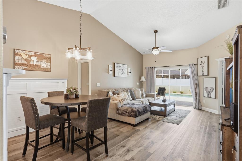 A dining area and living room with wood-look flooring, vaulted ceilings, and a sliding glass door — 844 WOODSONG WAY, CLERMONT, FL