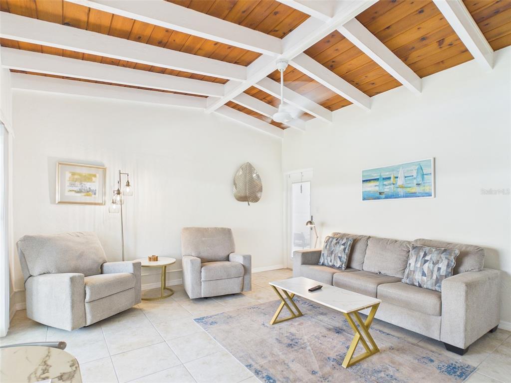 A living room features a vaulted wood-beamed ceiling, tile flooring, and neutral-toned furniture — 6006 MIDNIGHT PASS ROAD UNIT 51, SARASOTA, FL
