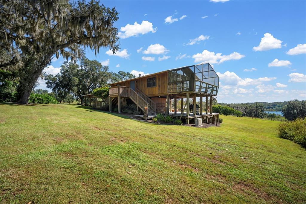 A wooden house with a screened-in porch stands on a grassy hill near trees — 32854 LISTER ROAD, DADE CITY, FL