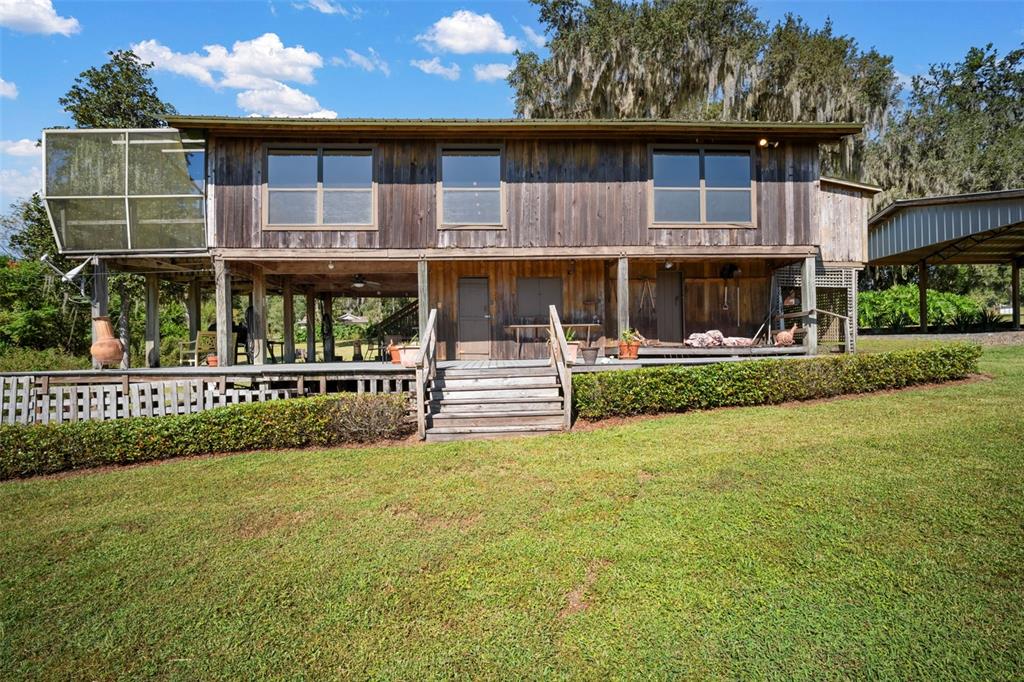 A two-story wooden house on stilts features a large deck, stairs, and a screened porch — 32854 LISTER ROAD, DADE CITY, FL