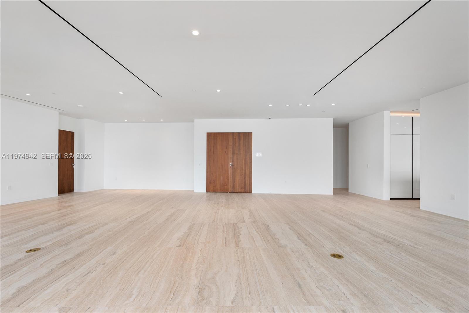 A spacious, minimalist room features white walls, recessed lighting, and light-toned stone flooring — 5 Grove Isle Dr # S201, Miami FL 33133, MIAMI, FL