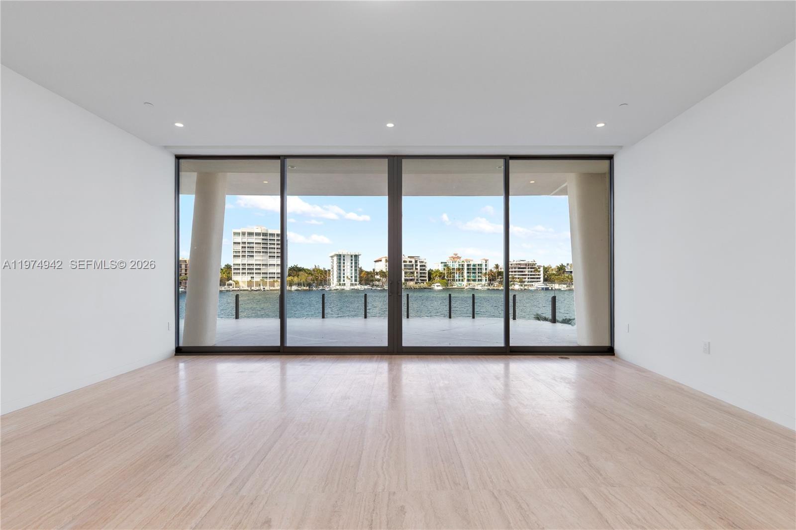An empty room with light wood flooring and large sliding glass doors overlooking water — 5 Grove Isle Dr # S201, Miami FL 33133, MIAMI, FL