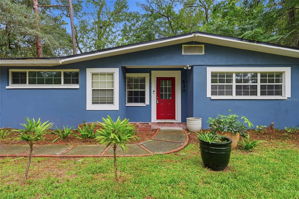 A blue single-story house features a red front door, white trim, and a curved walkway — 630 NW 35TH TERRACE, GAINESVILLE, FL