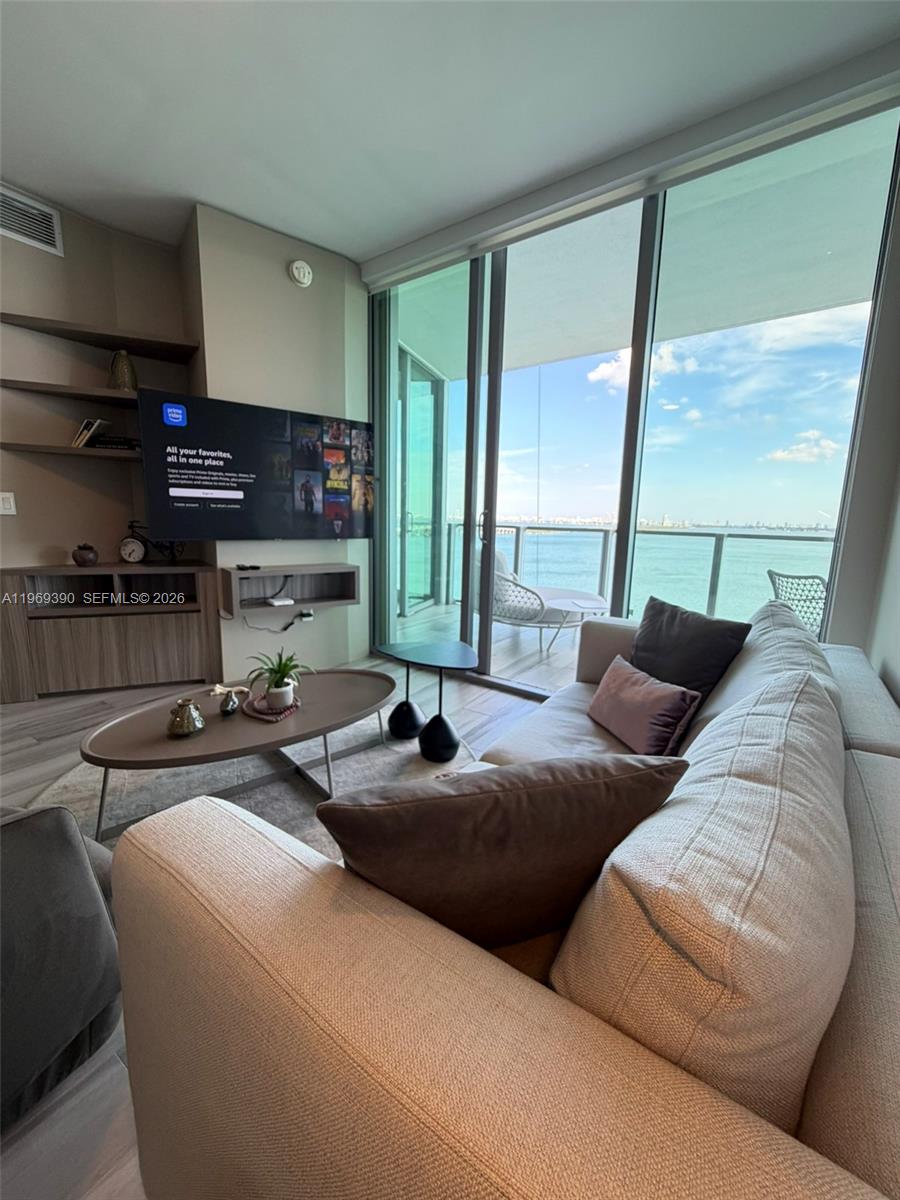 A modern living room features a sofa, television, and floor-to-ceiling windows overlooking the ocean — 2900 NE 7th Ave # 1205, Miami FL 33137, MIAMI, FL