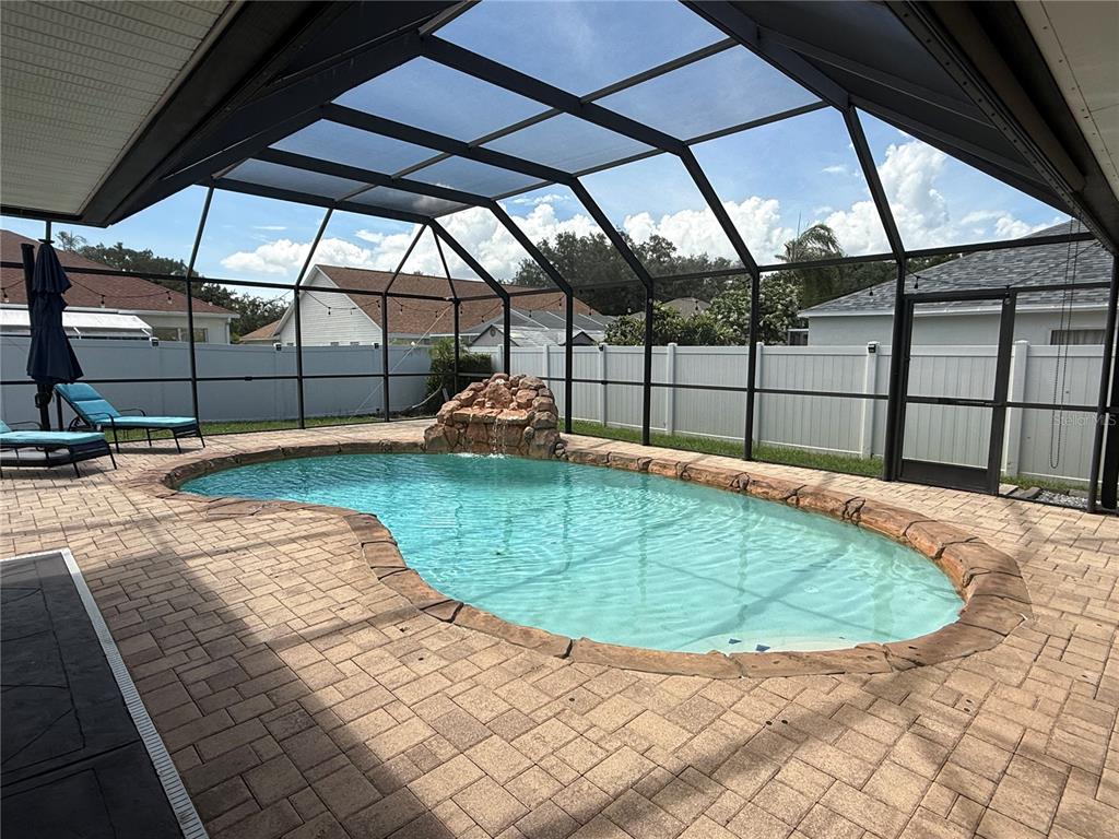 A screened-in patio features a kidney-shaped swimming pool with a rock waterfall and pavers — 2210 TOWERING OAKS CIRCLE, SEFFNER, FL
