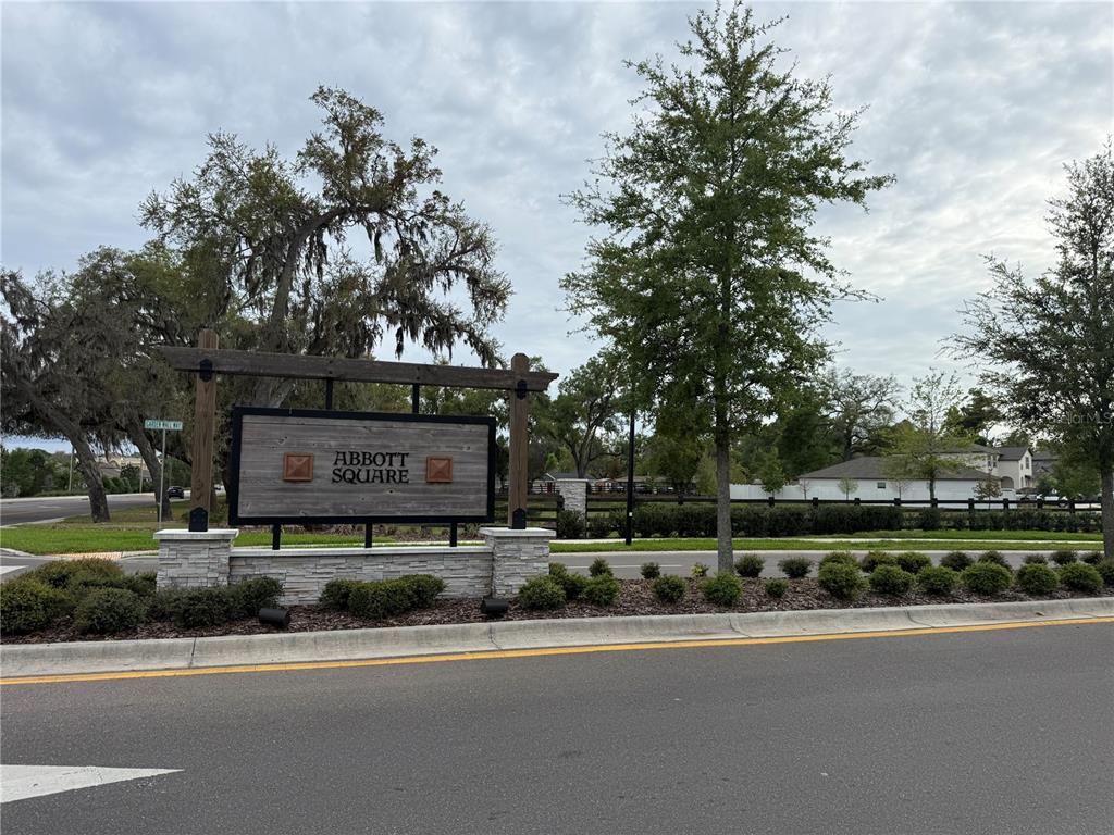 A wooden sign for Abbott Square stands behind a stone base and landscaped bushes — 36370 WELL HILL WAY, ZEPHYRHILLS, FL