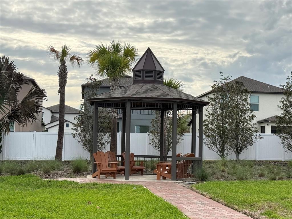 A dark-framed gazebo with Adirondack chairs sits on a brick path in a residential yard — 36370 WELL HILL WAY, ZEPHYRHILLS, FL