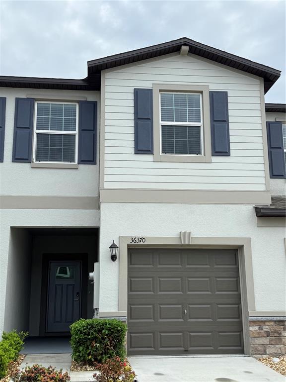 A two-story townhouse features a gray garage, a recessed front door, and light-colored siding — 36370 WELL HILL WAY, ZEPHYRHILLS, FL