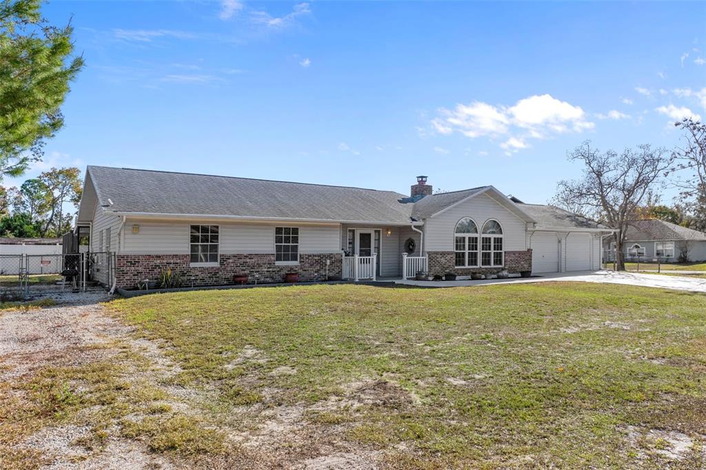 A single-story house with light siding, brick accents, and an attached garage under a blue sky — 4286 BLUEWATER AVENUE, SPRING HILL, FL