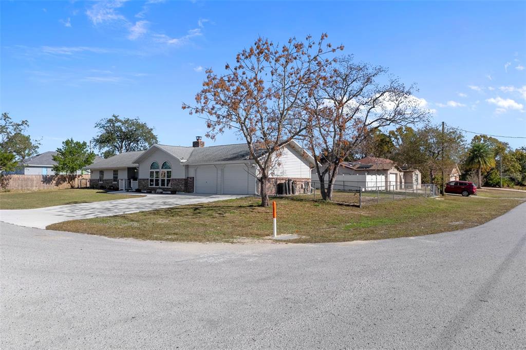 A single-story house with a two-car garage sits on a corner lot with trees — 4286 BLUEWATER AVENUE, SPRING HILL, FL