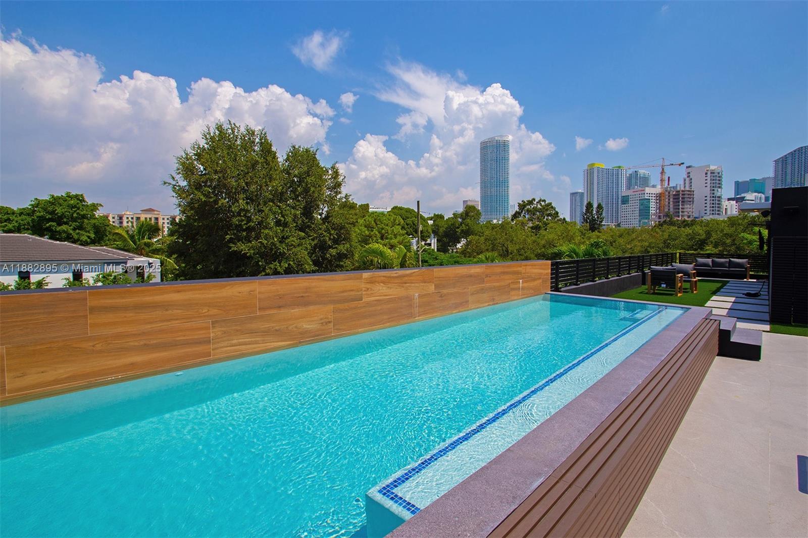 An elevated rectangular swimming pool features wood-look tile siding and overlooks a city skyline — 420 SW 15th Rd, Miami FL 33129, MIAMI, FL