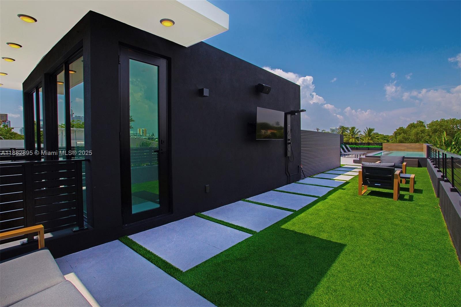 A modern rooftop terrace features artificial turf, stone pavers, a black wall with a television, and a pool — 420 SW 15th Rd, Miami FL 33129, MIAMI, FL