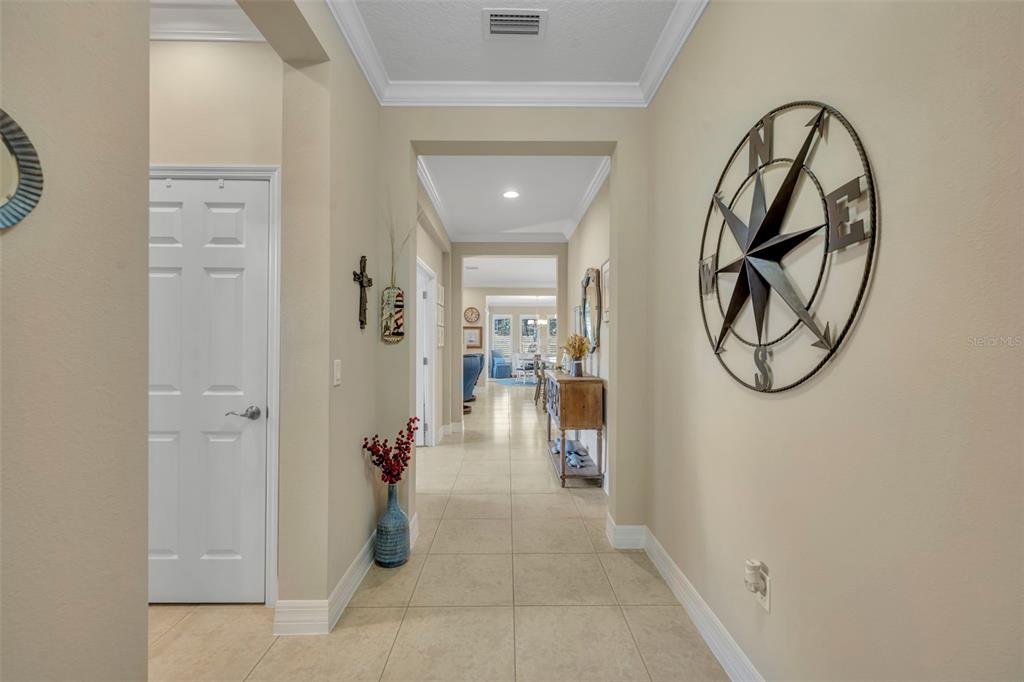 A tiled hallway features a large metal compass wall art and leads toward a living area — 115 SALT MARSH LANE, GROVELAND, FL
