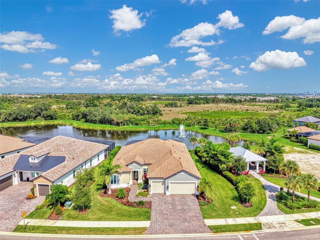 An aerial view shows a suburban house with a tiled roof, driveway, and backyard pond — 18045 HOME RUN DRIVE, VENICE, FL