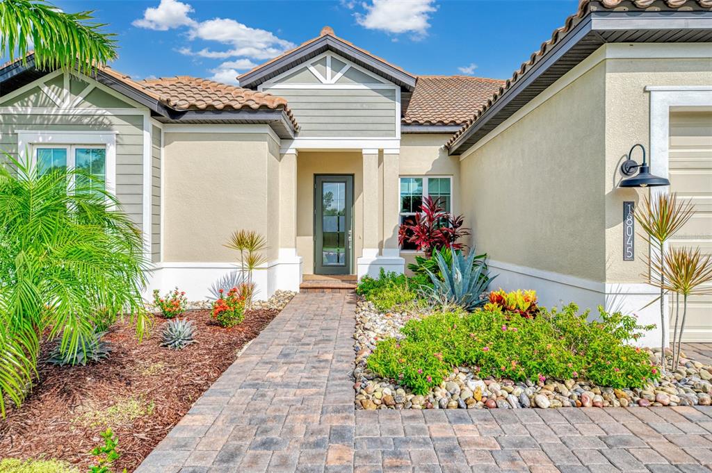 The exterior of a single-story house features a stone walkway, landscaping, and a tiled roof — 18045 HOME RUN DRIVE, VENICE, FL