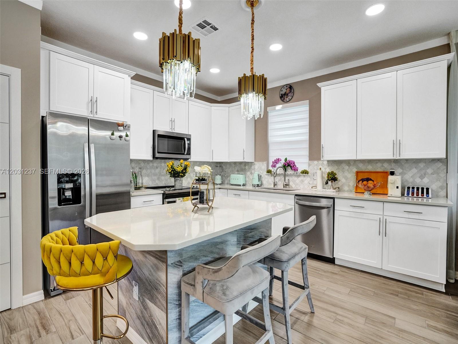 A modern kitchen features white cabinetry, a marble-patterned island, and gold-accented pendant lighting — 4414 Ficus St, Hollywood FL 33021, HOLLYWOOD, FL
