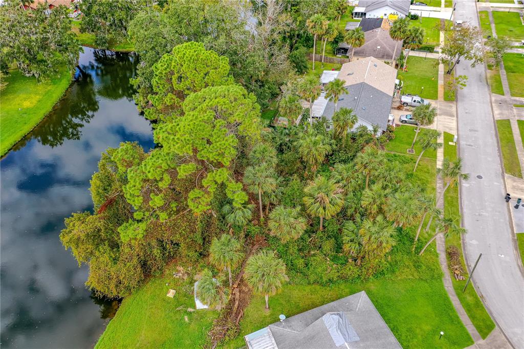 An aerial view shows a residential property with a canal, dense trees, and nearby houses — TBD TUMBLEWEED TRAIL, PORT ORANGE, FL