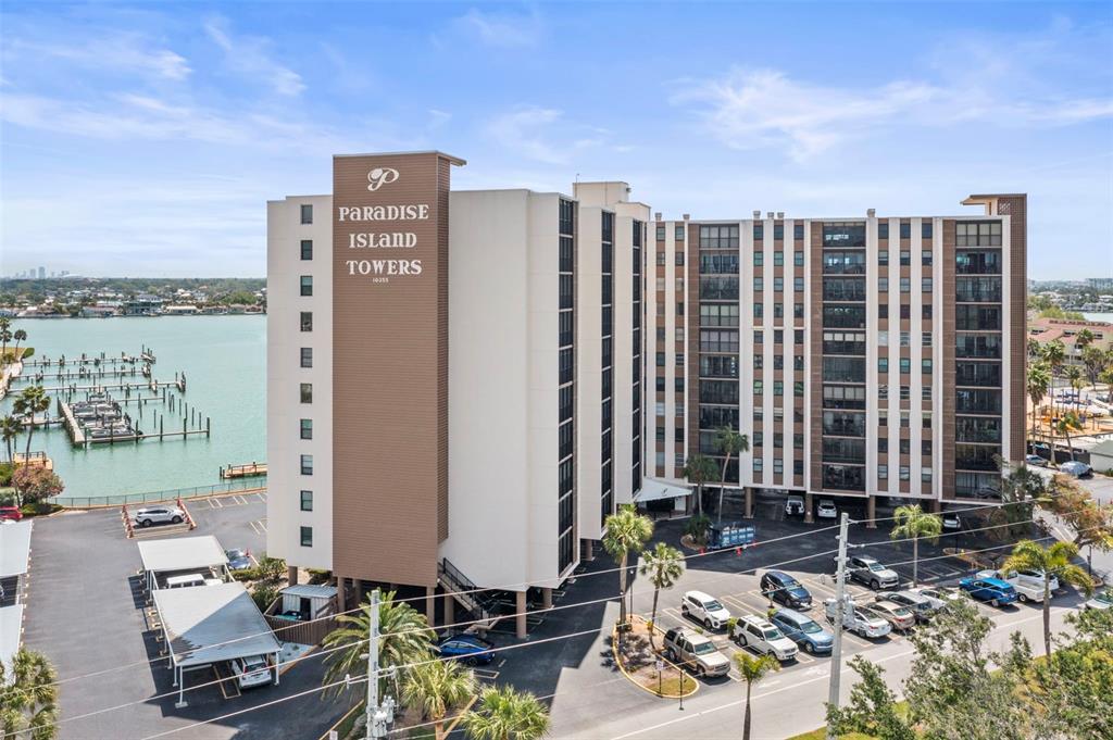 An exterior view of a multi-story apartment building with a marina and parking lot — 10355 PARADISE BOULEVARD UNIT 403, TREASURE ISLAND, FL