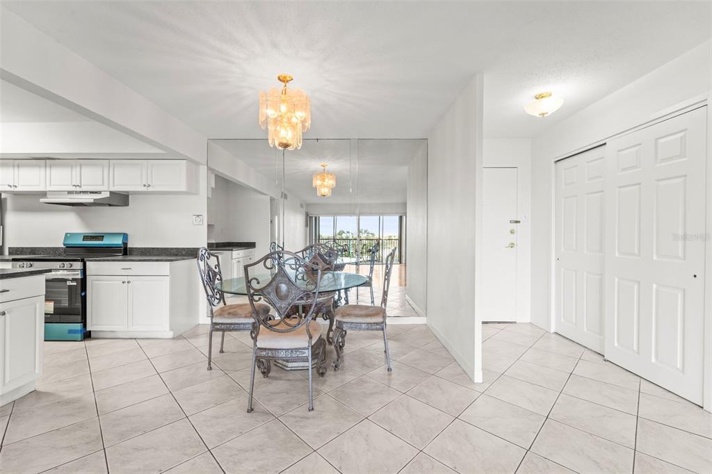 A dining area with a glass table, ornate chairs, mirrored wall, and adjacent white kitchen — 10355 PARADISE BOULEVARD UNIT 403, TREASURE ISLAND, FL