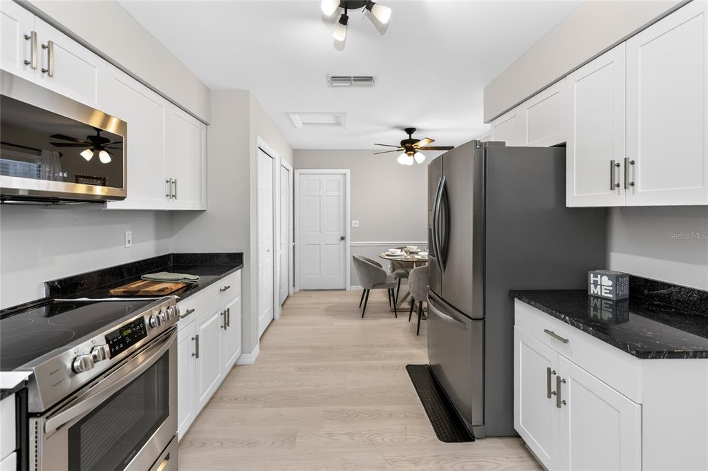 A kitchen with white cabinets, black countertops, and stainless steel appliances leads to a dining area — 172 DEER LAKE CIRCLE, ORMOND BEACH, FL