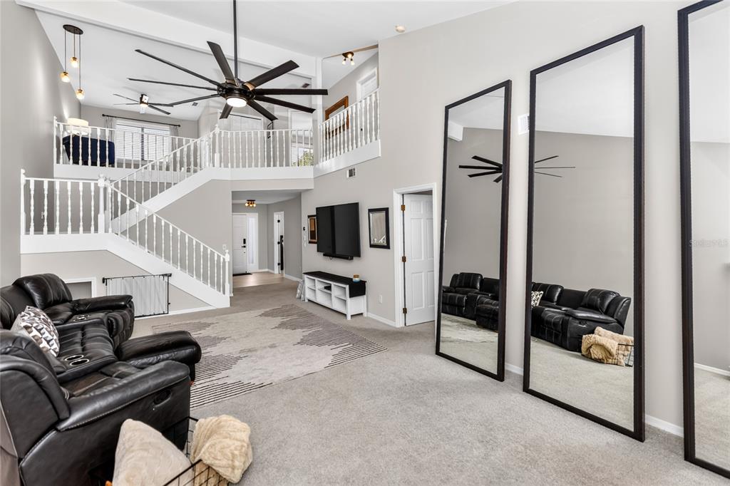 A living room with a staircase, a large ceiling fan, and three tall floor mirrors — 172 DEER LAKE CIRCLE, ORMOND BEACH, FL