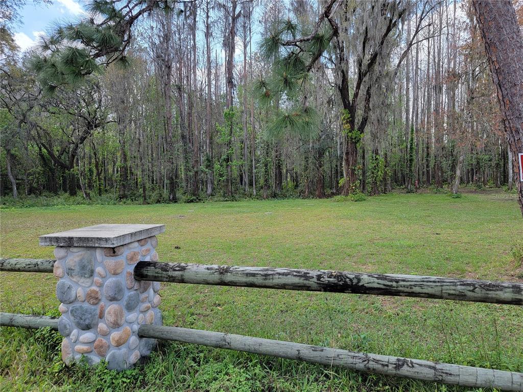 A grassy lot is bordered by a wooden fence with a stone pillar in the foreground — TBD BELL LAKE ROAD, LAND O LAKES, FL